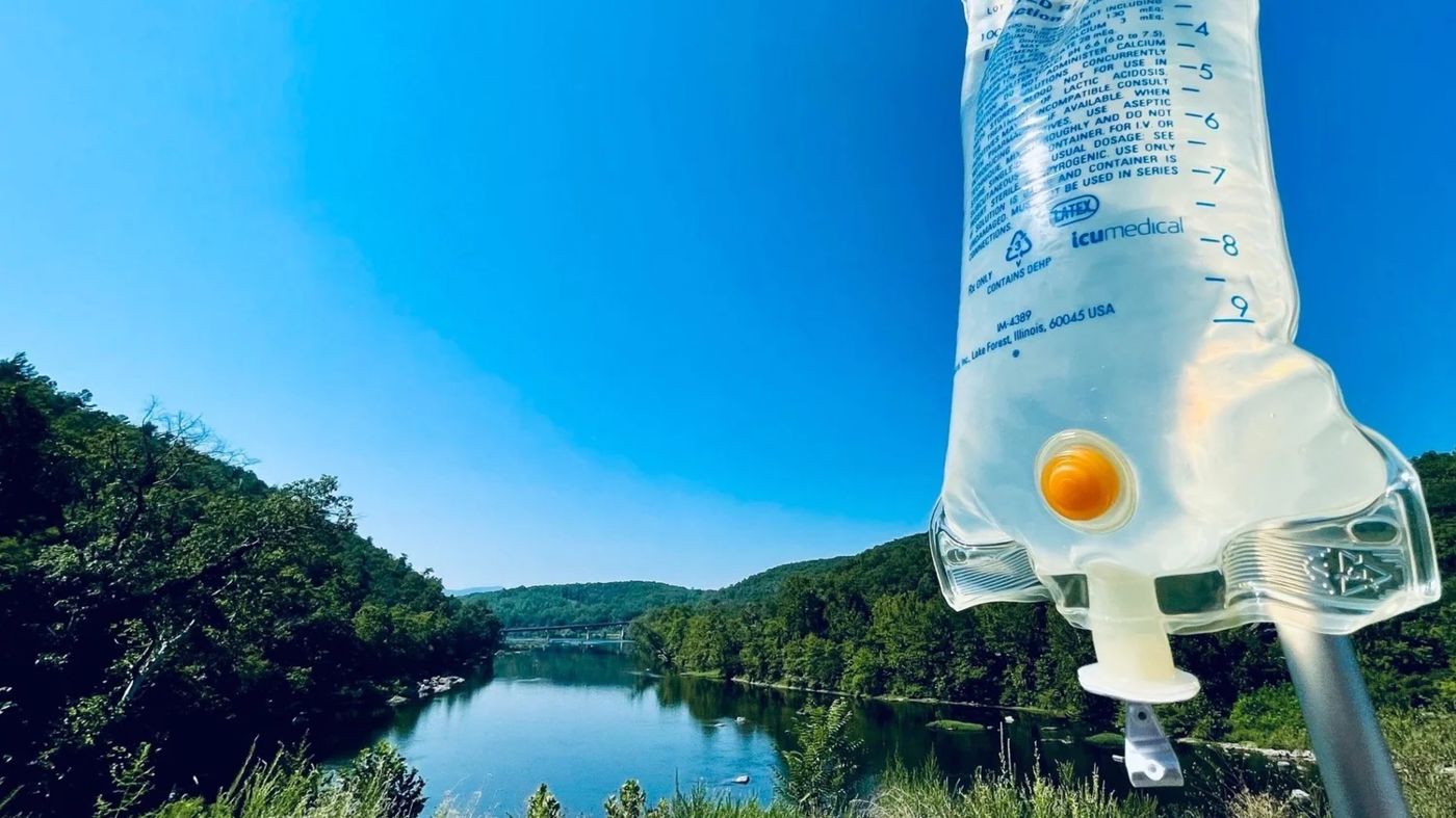 IV drip bag outdoors with a lake and trees behind it